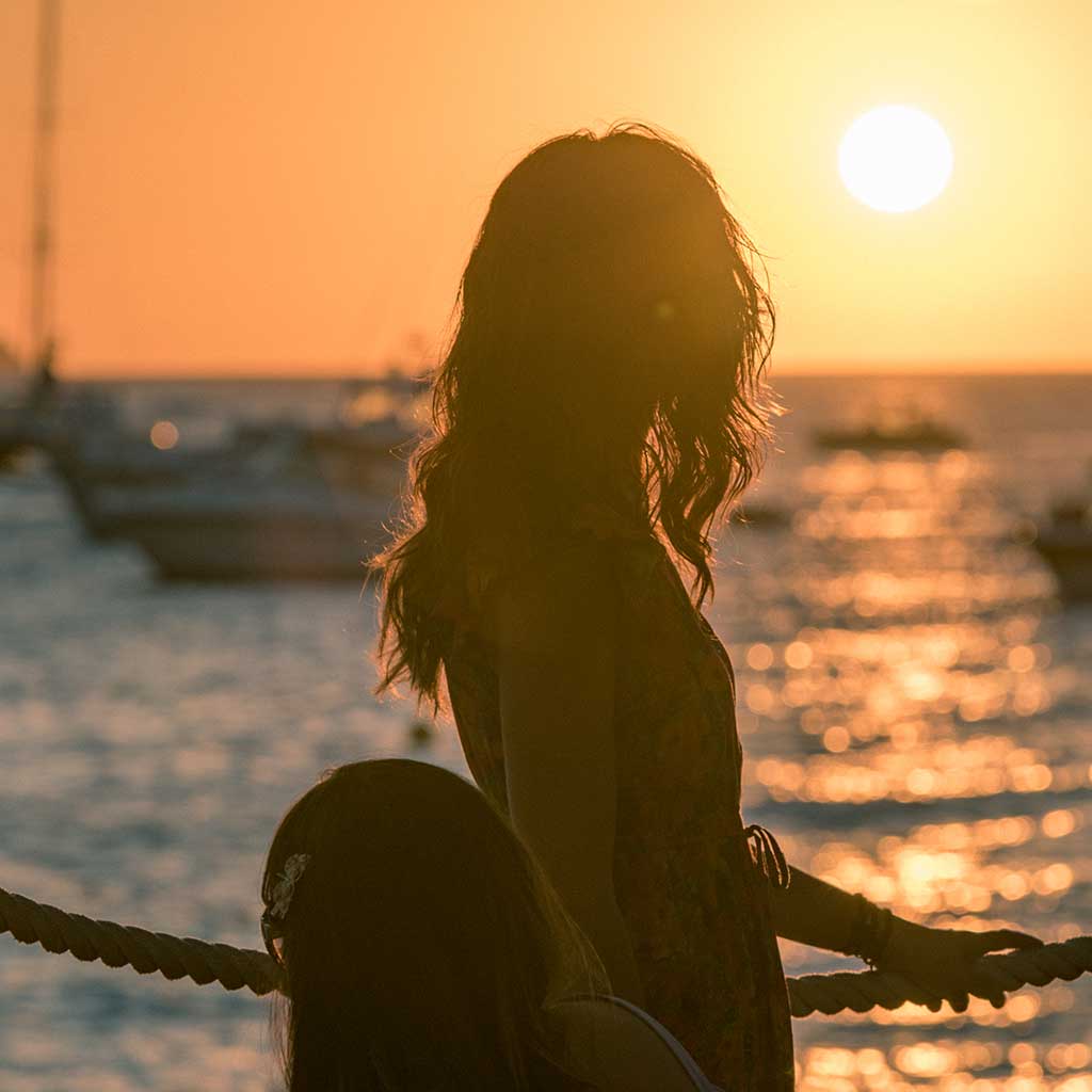 A girl standing near her table at Café del Mar and watching the sunset over the sea